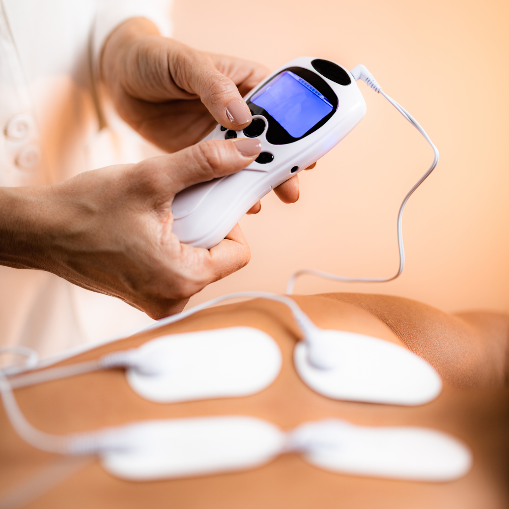 Nahaufnahme einer Person, die ein TENS-Gerät (Transkutane Elektrische Nervenstimulation) mit Elektroden auf der Haut bedient, um Schmerzen zu lindern oder Muskeln zu stimulieren.