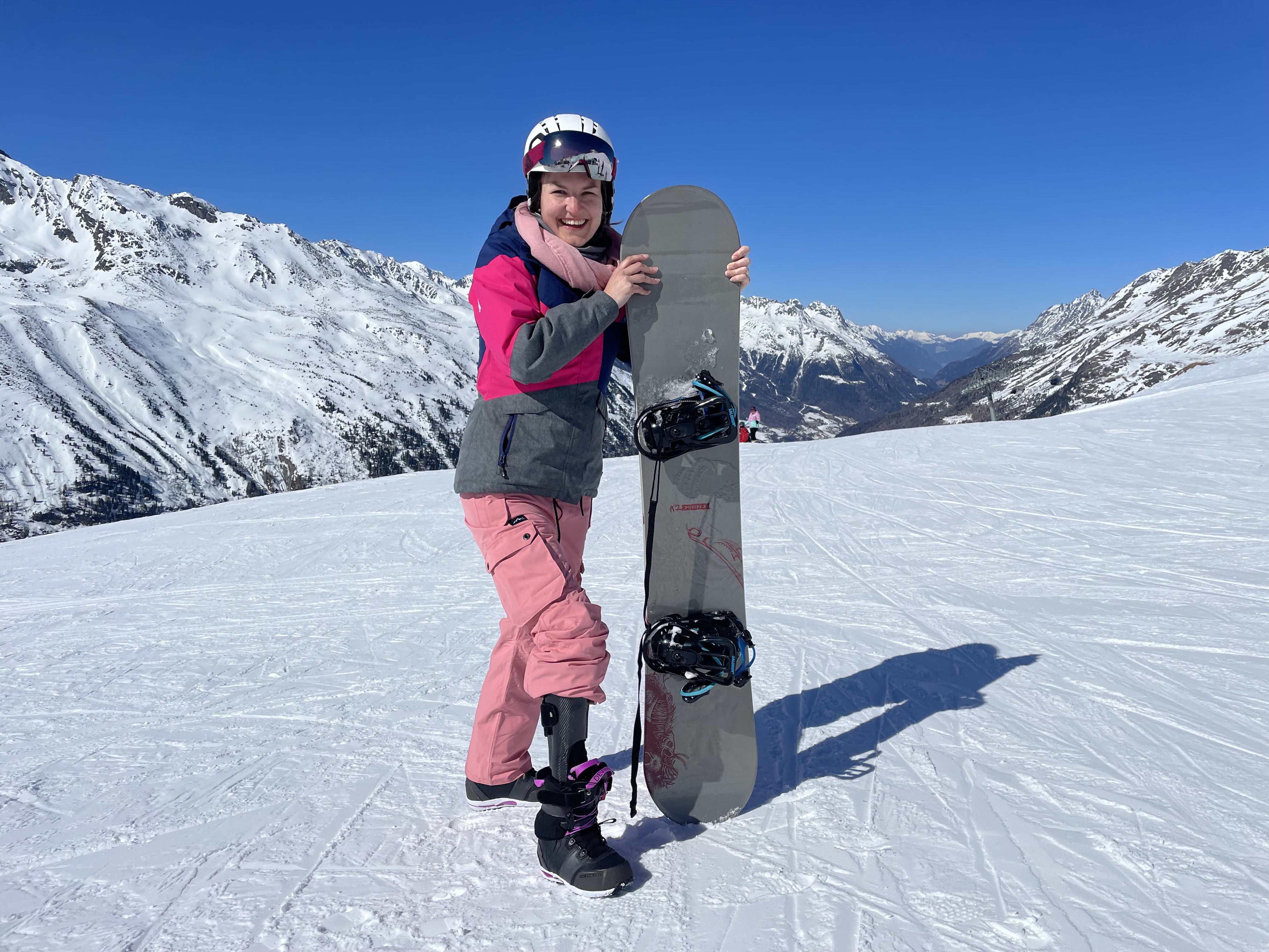 Kundin Laura von Mitschke posiert lächelnd auf der Piste mit ihrem Snowboard.