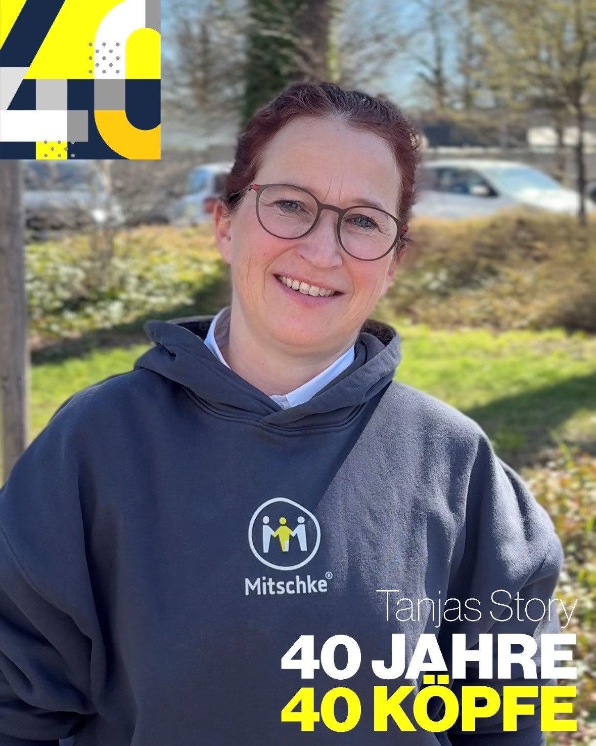 Frau mit Brille in blauem Mitschke-Hoodie steht im Grünen und lächelt freundlich 