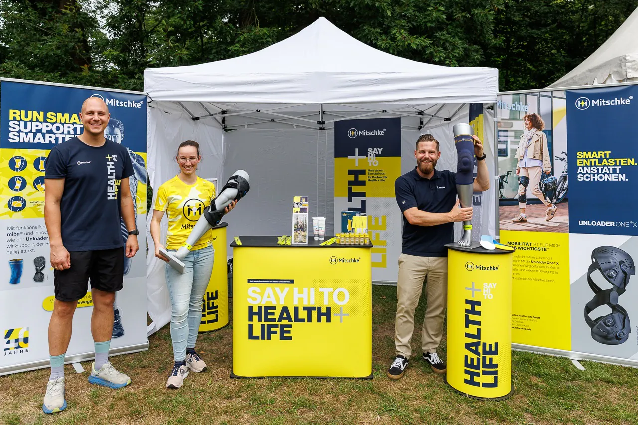 drei lächelnde Mitarbeitende präsentieren Bandagen und Orthesen am gelb-blauen Mitschke Health + Life Stand bei Gt läuft 2026